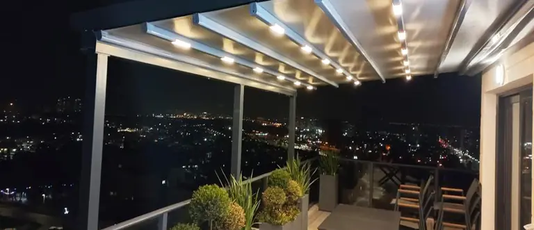 פרגולה חשמלית מבד עם תאורה מובנית במרפסת גג בעכו בלילה